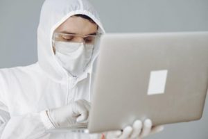 A man in a white protective suit working on a laptop.