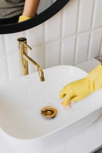 a person in yellow gloves cleaning a sink in the bathroom