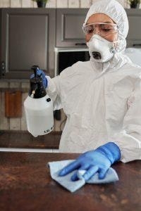 A person in a protective suit is disinfecting a surface.