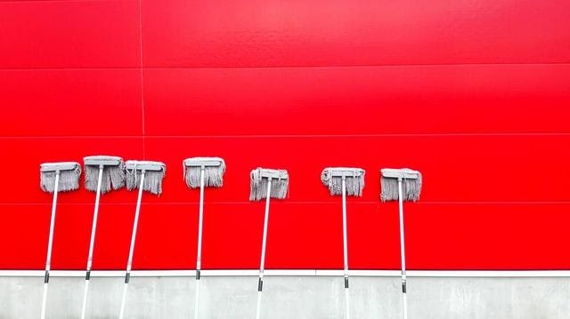 seven cleaning mops against a red wall
