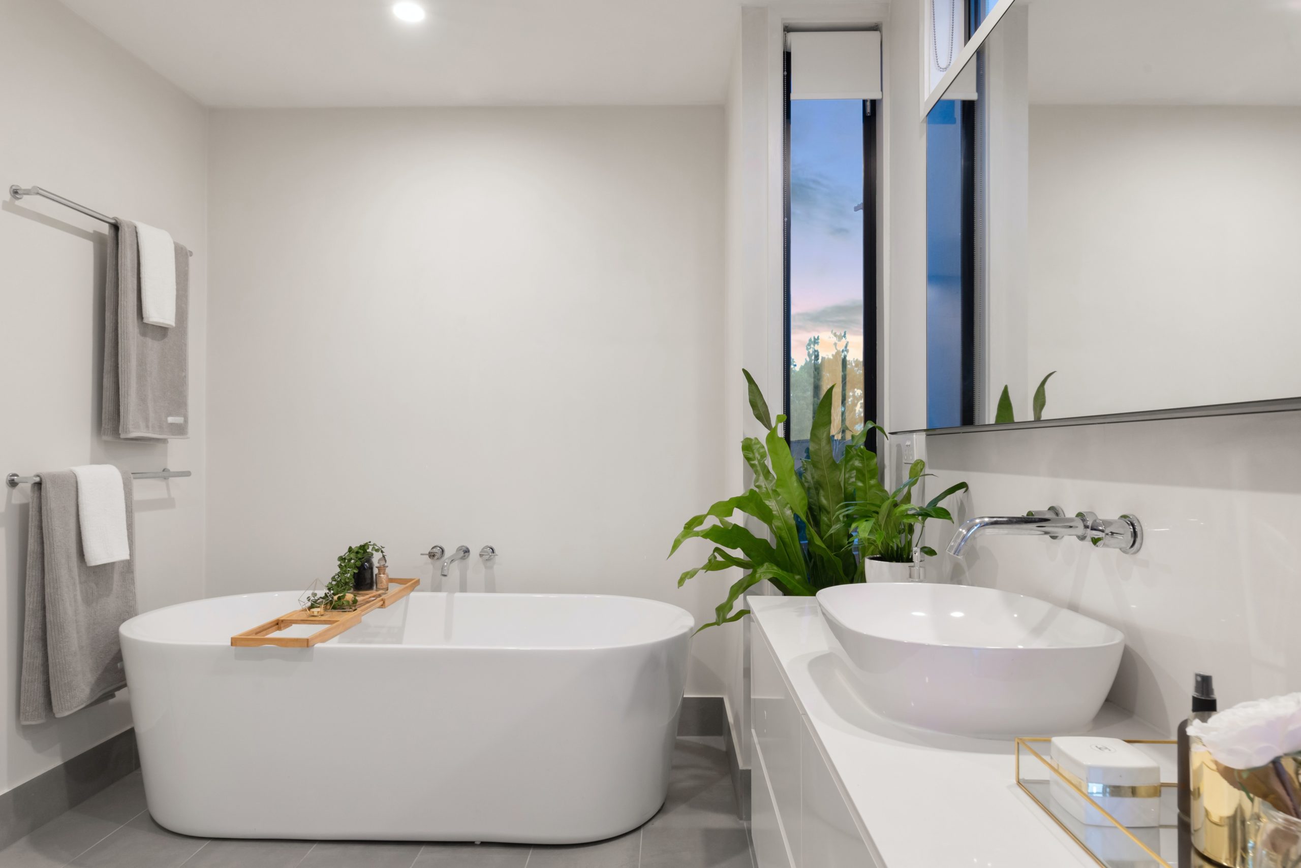 A white bathroom with a ceramic bathtub, sink, and grey towels